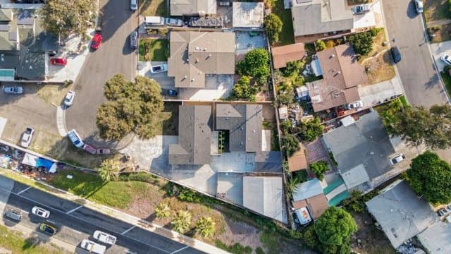 Aerial view of a residential property with multiple buildings (a main house, ADU, and studio) on a single lot, surrounded by other homes and a street.